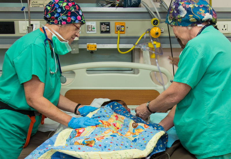 PACU nurses Ellen Adams and Marilyn Perkins monitor a patient following surgery and comfort him with a hand-crafted quilt.